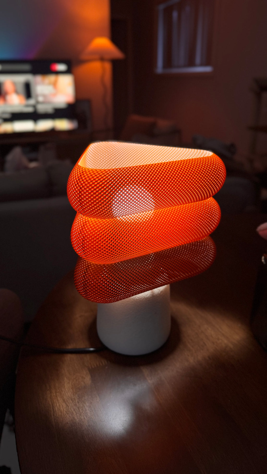 Modern lamp with orange mesh design on a wooden surface in a dimly lit room.